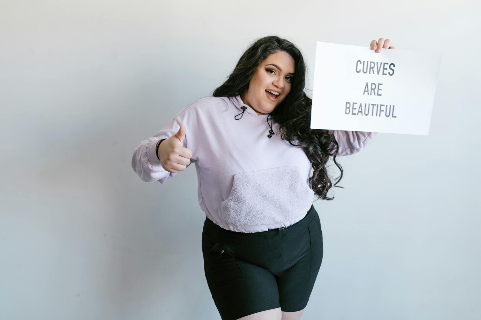 Stylizacje plus size na co dzień: jak łączyć wygodę i modę w większym rozmiarze Uśmiechnięta kobieta plus size trzymająca tabliczkę Curves Are Beautiful